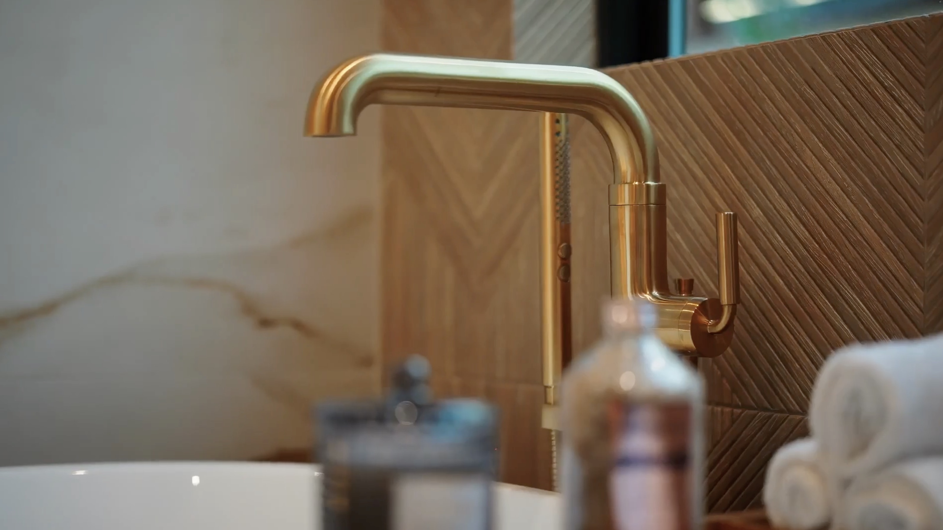 Close detail of a brushed brass kitchen faucet and textured wood backsplash